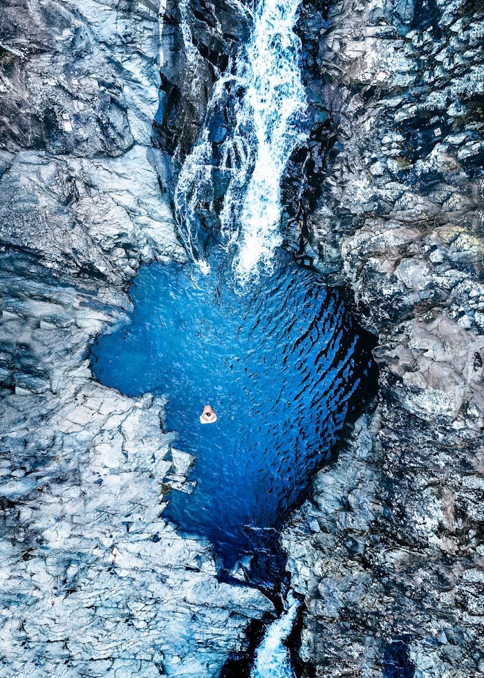 Stunning aerial shot of a crystal-clear blue waterfall pool surrounded by rocky terrain in Australia.